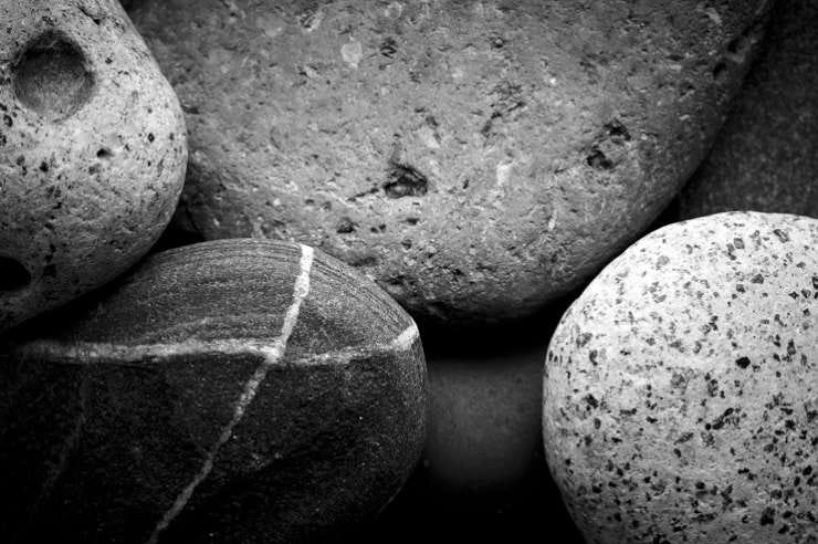 A close-up monochrome image of assorted smooth rocks with different textures and patterns.