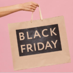 Adult arm holding Black Friday shopping bag on pink backdrop.