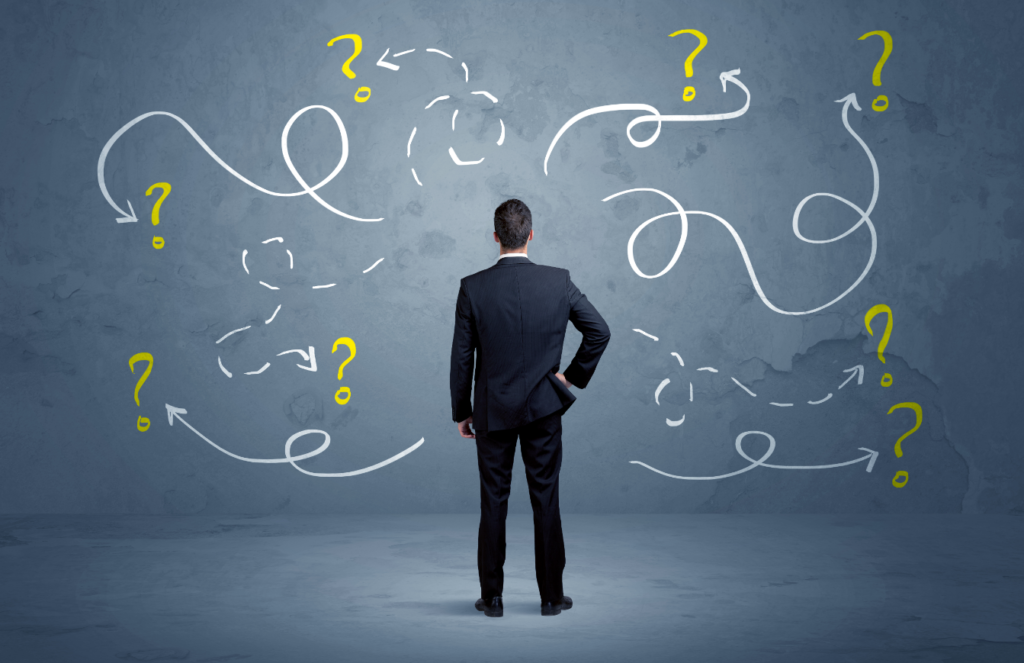 A businessman with hands on hips looking at a wall with drawn question marks and arrows suggesting confusion and decision making.