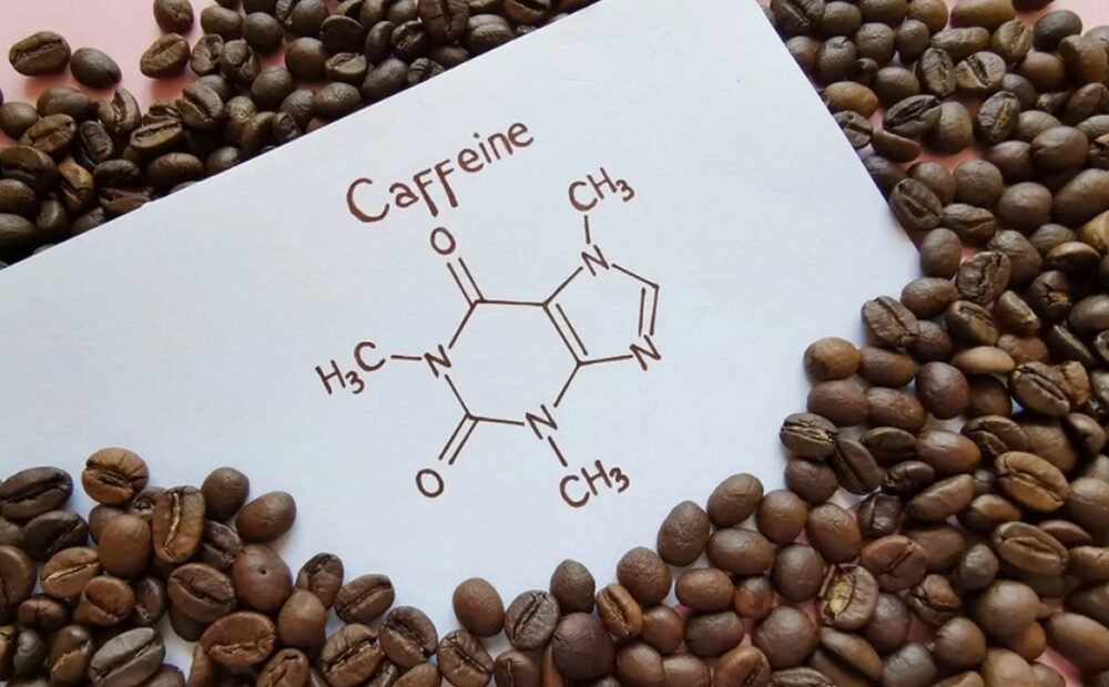 A piece of paper with the chemical structure of caffeine drawn on it, surrounded by scattered coffee beans on a pink surface.