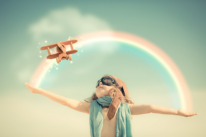 Child playing pilot under rainbow with toy plane, evoking childhood imagination and adventure.