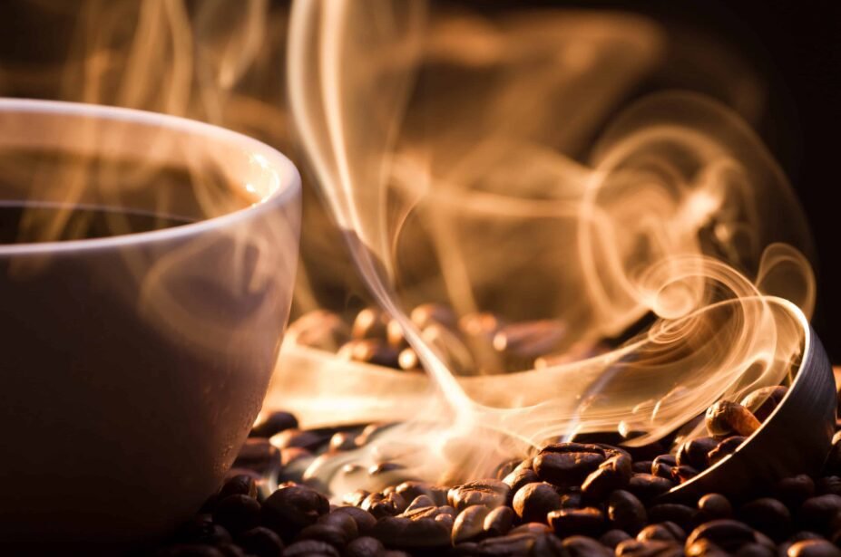 A warm-toned image featuring a close-up of a white coffee cup with steam gracefully rising above it, nestled among roasted coffee beans.