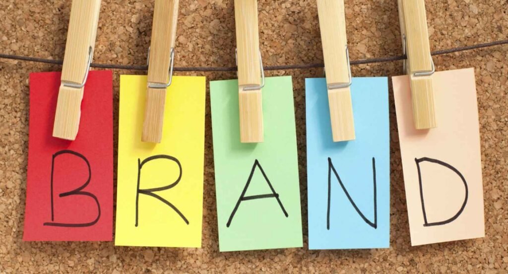 Coloured notes with the letters 'BRAND' written across them, pegged onto a string against a cork board background.