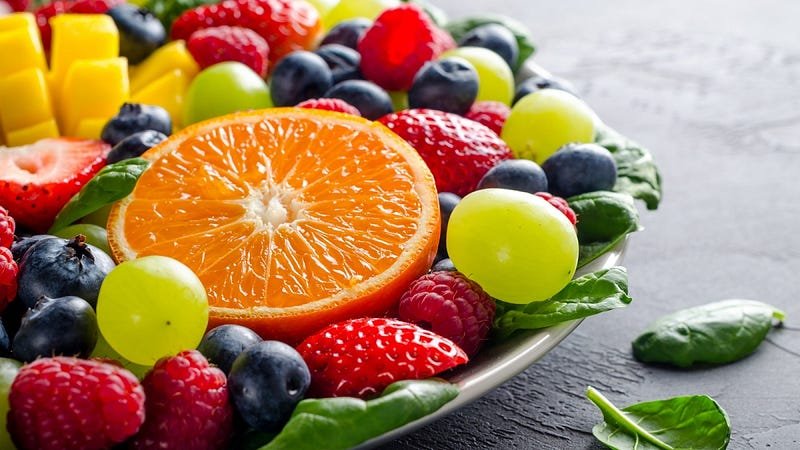 Colorful fresh fruit plate on dark background, showcasing vibrant colors and textures.