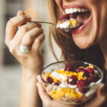 Person delightfully eating vibrant fruit and yogurt bowl in a cozy setting.