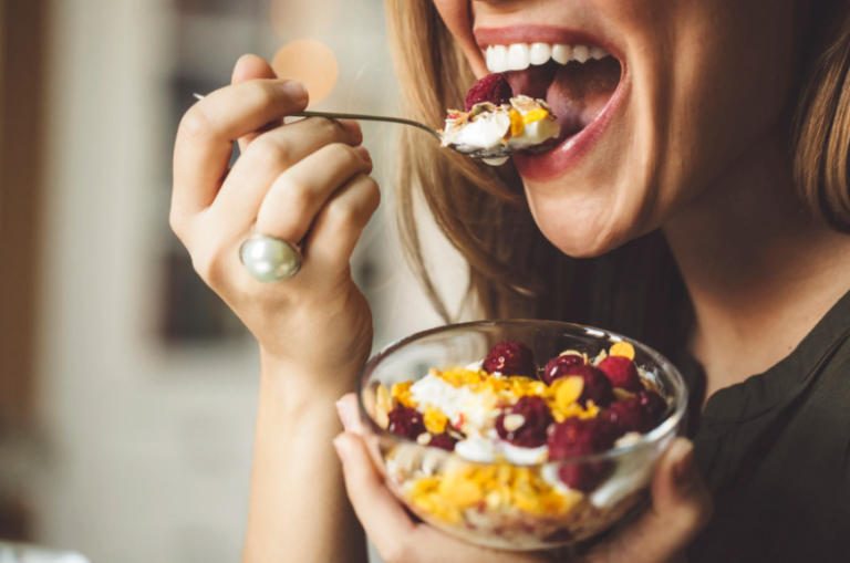 Person delightfully eating vibrant fruit and yogurt bowl in a cozy setting.