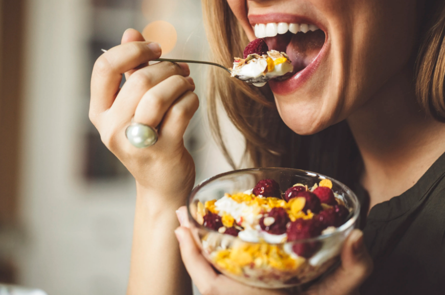 Person delightfully eating vibrant fruit and yogurt bowl in a cozy setting.