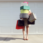 Person holding colorful gifts and shopping bags in front of white garage door.