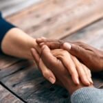 Tender moment: diverse hands clasped on wooden surface, conveying warmth, connection, and support.