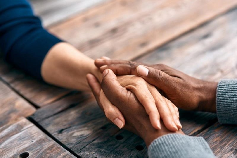 Tender moment: diverse hands clasped on wooden surface, conveying warmth, connection, and support.