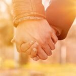 Close-up shot of two hands interlocked in golden hour sunlight, conveying intimacy and connection.
