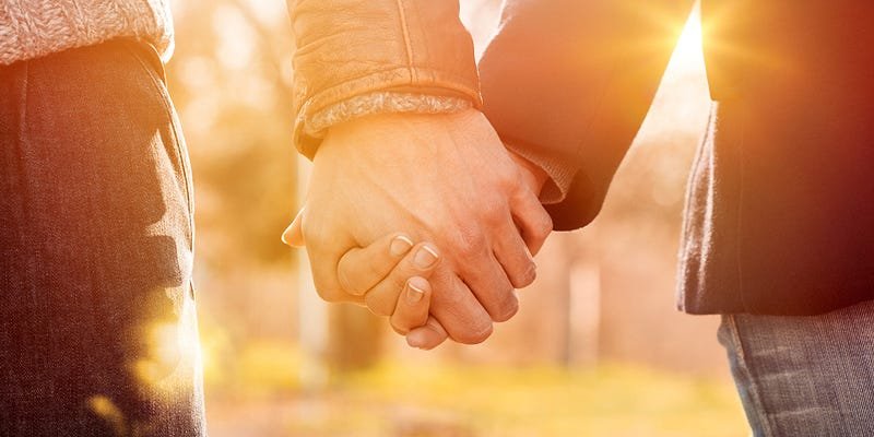 Close-up shot of two hands interlocked in golden hour sunlight, conveying intimacy and connection.