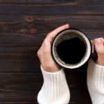 Cozy white sweater with black coffee mug on rustic wooden background.