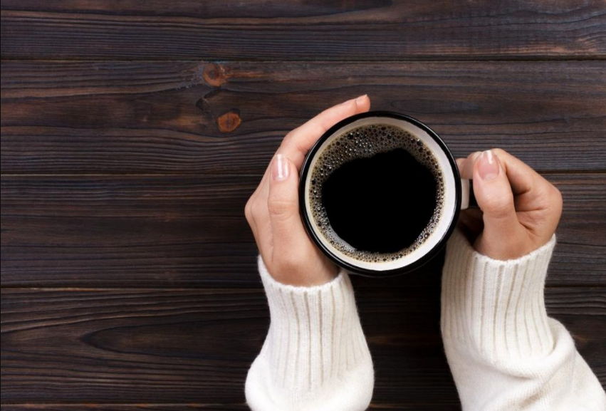 Cozy white sweater with black coffee mug on rustic wooden background.