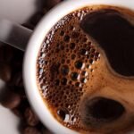 Freshly brewed coffee with crema and glossy beans on white saucer.
