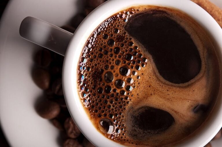 Freshly brewed coffee with crema and glossy beans on white saucer.