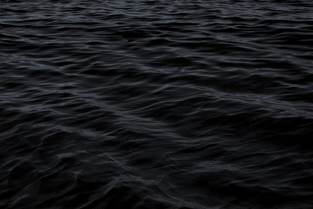 A dark, textured expanse of water with ripples and subtle waves, implying a vast and calm ocean or sea.