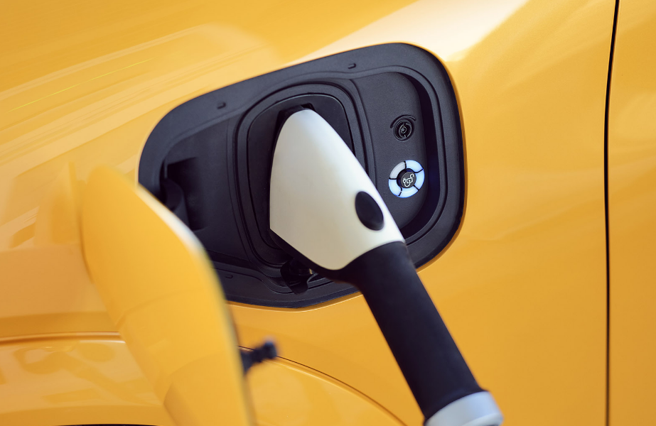 A close-up of an electric vehicle's charging port with a plugged-in charging cable, situated on a vibrant yellow car exterior.