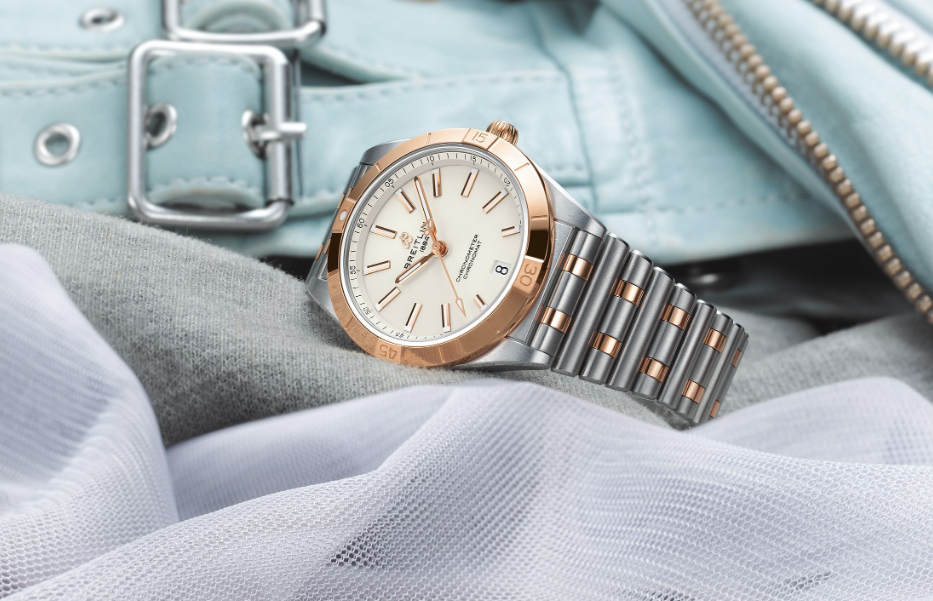 A luxury two-tone wristwatch with a rose gold bezel and crown, and a linked silver and rose gold bracelet, displayed on a draped gray cloth with a pale blue leather bag in the background.