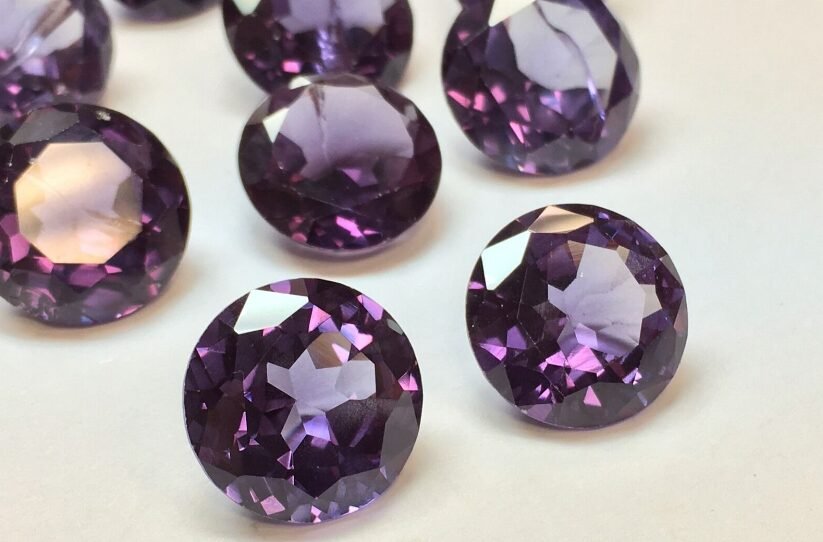 A collection of faceted round amethyst gemstones scattered on a white surface, with focus on one prominent stone in the foreground.