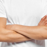 Crossed arms pose in white t-shirt against grey background.