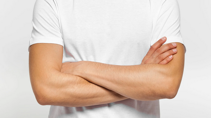 Crossed arms pose in white t-shirt against grey background.