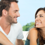 Couple sharing joy and laughter, sitting close with warm smiles, in a serene outdoor setting.