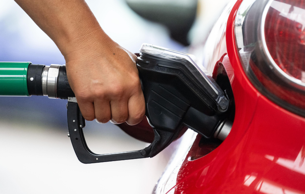 Person refueling red car at gas station, holding black fuel nozzle.