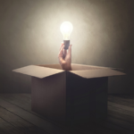 Mysterious hand holding glowing light bulb in open box illuminating dim room.