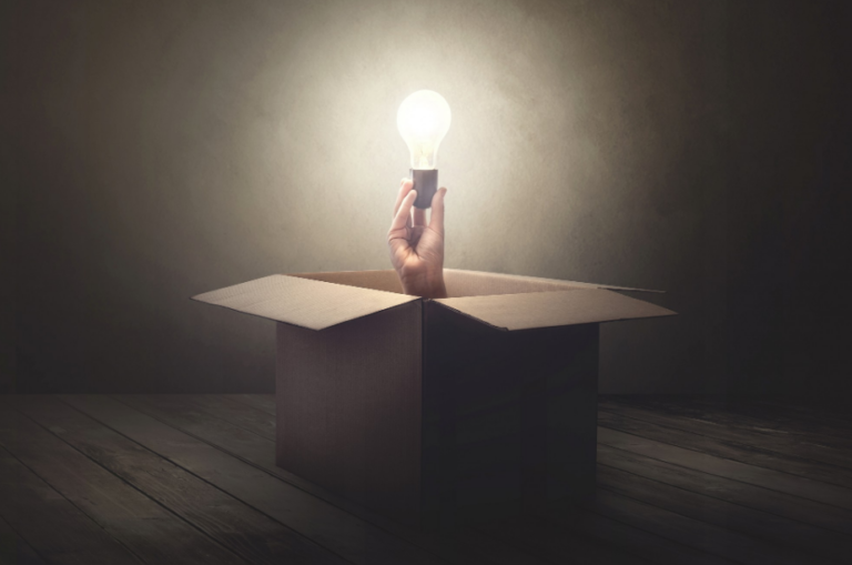 Mysterious hand holding glowing light bulb in open box illuminating dim room.