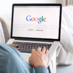Person browsing Google on laptop in cozy home environment.