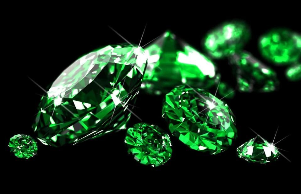 Several shiny green gemstones of different sizes scattered on a black surface.