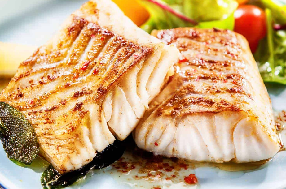 Grilled fish fillets with grill marks, served with salad and herbs on a white plate.