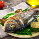 Grilled whole fish with lemon, snow peas, and tomatoes on rustic table.