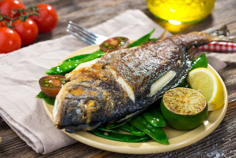 Grilled whole fish with lemon, snow peas, and tomatoes on rustic table.