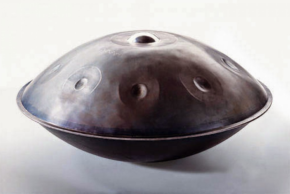 A handpan musical instrument with multiple indentations, resting on a white background.