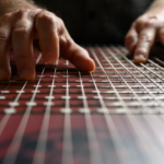 Person adjusting faders on digital mixing board in studio setting with dramatic lighting.