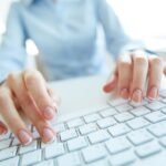 Person typing on white keyboard in modern office, showcasing productivity and technology use.