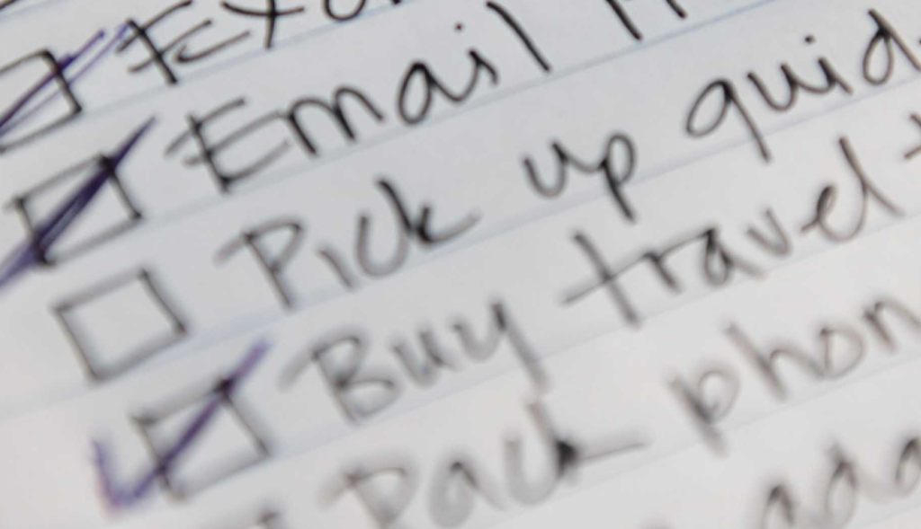 Close-up of a handwritten to-do list with items ticked off, slightly blurred, on a lined paper.