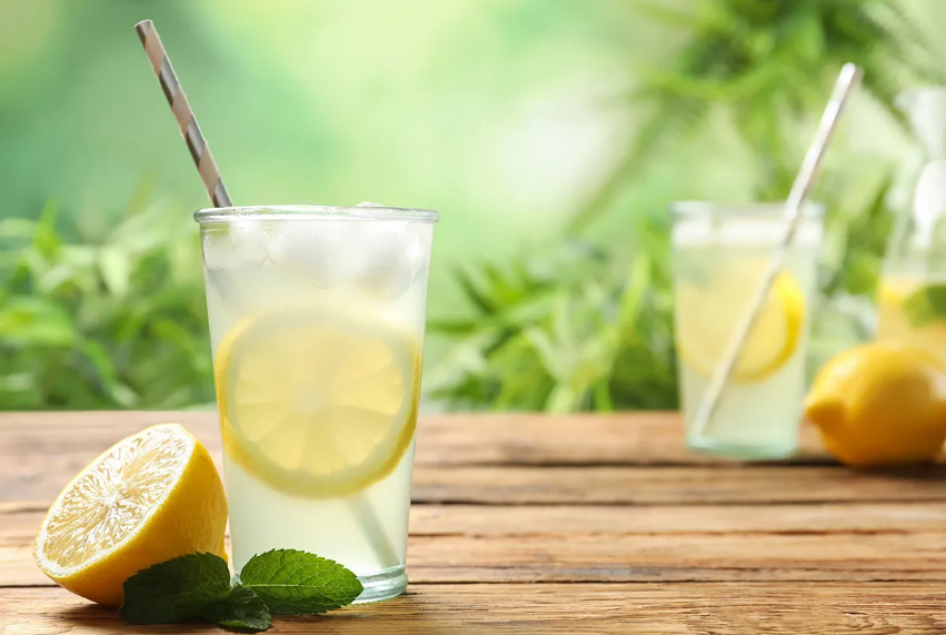 Refreshing lemonade drinks on wooden table with mint and lemon slices, outdoor relaxation vibe.