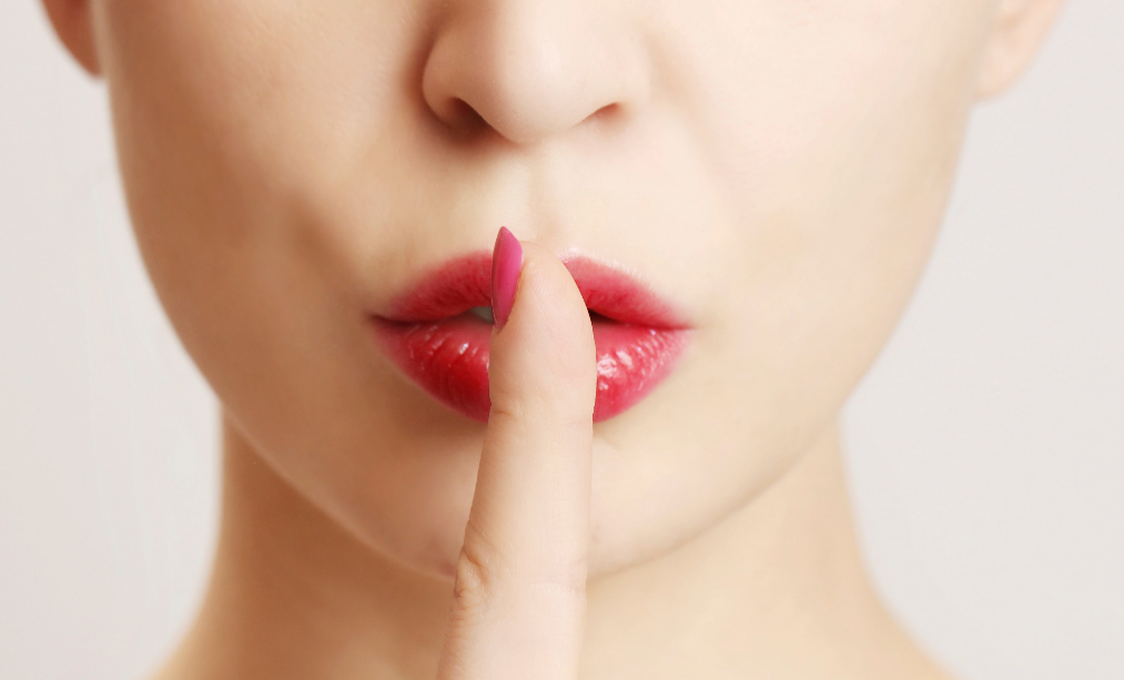Silent gesture: hushed secret with red lips and finger to lips.