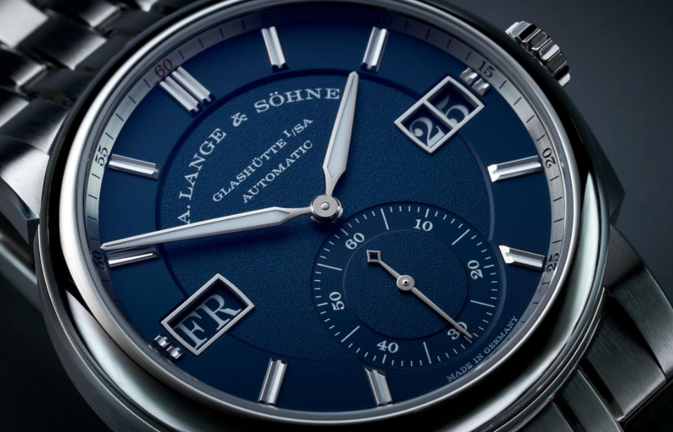 Close-up of an A. Lange & Söhne luxury wristwatch with a blue dial, silver-tone case, hands, and markers, featuring day and sub-seconds dials.