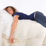 Woman resting on bed with alarm clock, creating a tranquil atmosphere.