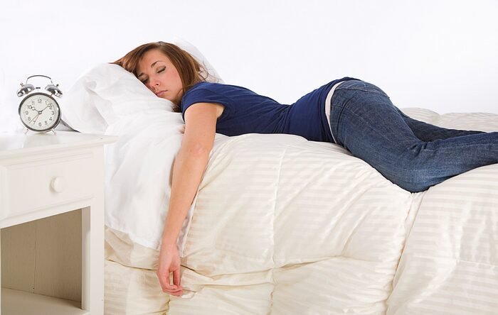 Woman resting on bed with alarm clock, creating a tranquil atmosphere.