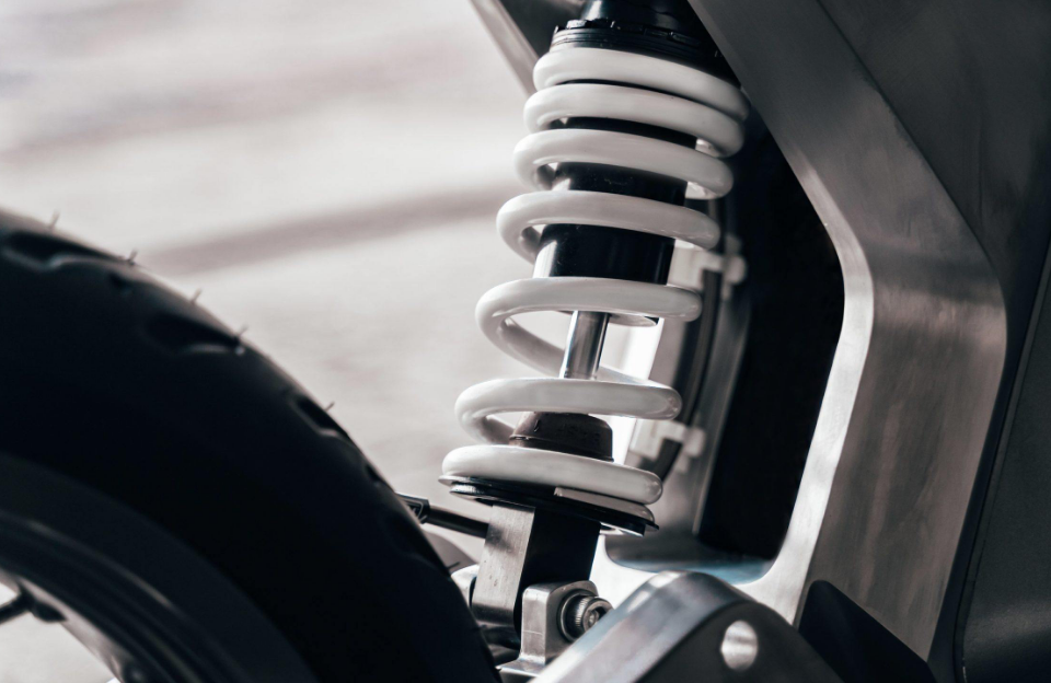 Close-up of a white motorcycle shock absorber and spring assembly with the wheel partially visible in the foreground.