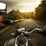 Motorcycle rider on scenic road at sunset, surrounded by lush countryside and golden sky.