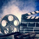 Classic filmmaking essentials: clapperboard and film reel against blue sky backdrop.