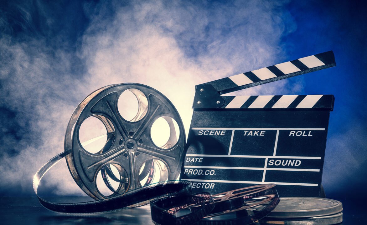 Classic filmmaking essentials: clapperboard and film reel against blue sky backdrop.