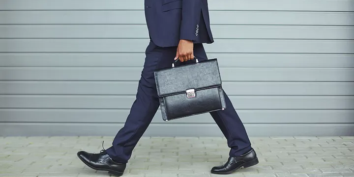 Business professional in navy suit strides with leather briefcase, exuding professionalism and elegance.