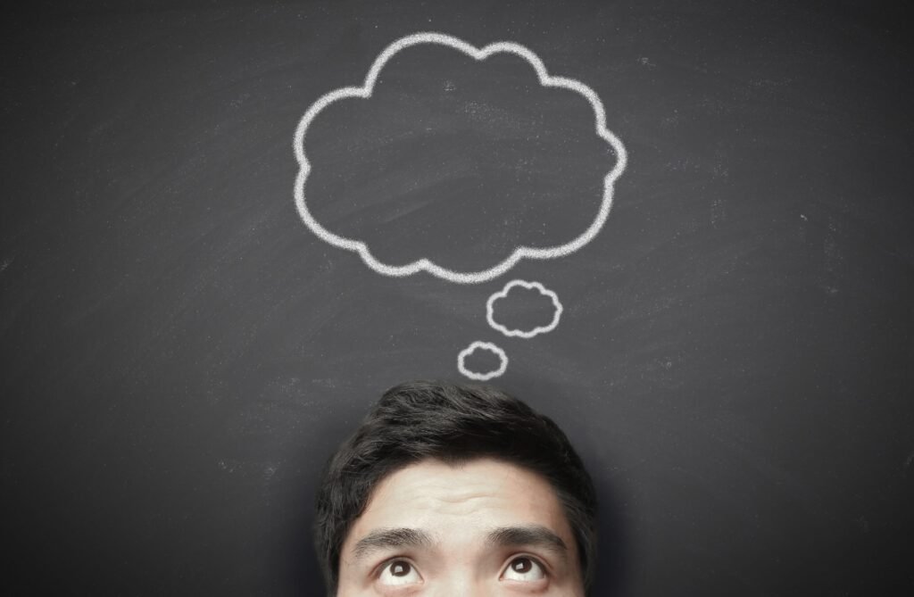 A person's forehead and eyes visible against a blackboard with a chalk-drawn thought bubble above their head.
